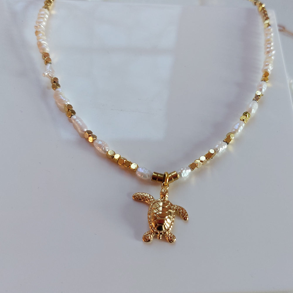 Detailaufnahme einer goldenen Schildkröten Halskette mit Perlen, filigraner maritimer Schmuck Anhänger